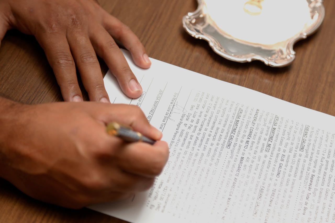 our-experience Hand signing a contract on a wooden desk, emphasizing business formalities.