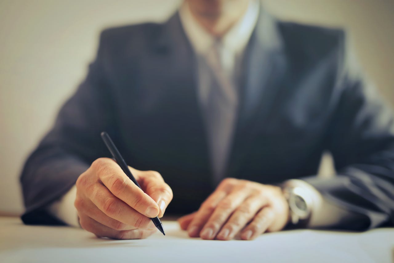 why-choose-us Male entrepreneur wearing formal suit sitting at table in workplace and signing documents while making successful business deal