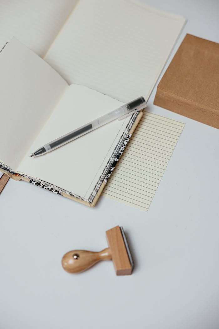 services-02 A minimalist workspace featuring an open notebook, pen, and wooden stamp on a white surface.