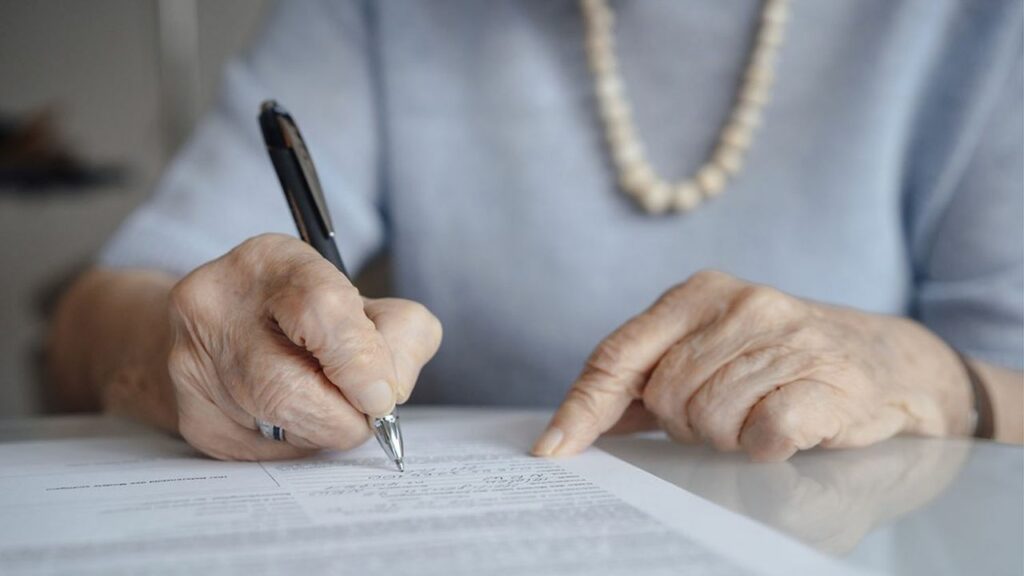 hands of senior woman writing on paper with pen